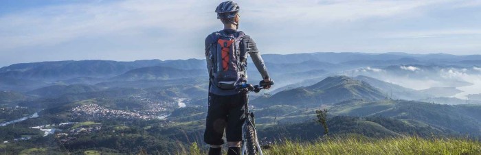 biker holding mountain bike on top of mountain with green grass